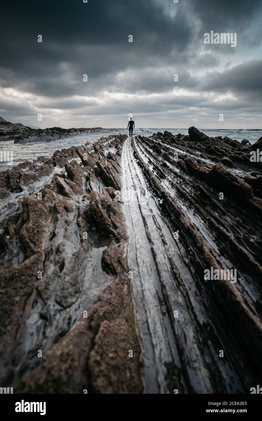 Silhouette der unkenntlich stehende Person auf rauhe felsige Oberfläche in der Nähe von Meer an bewölkten Tag Stockfoto