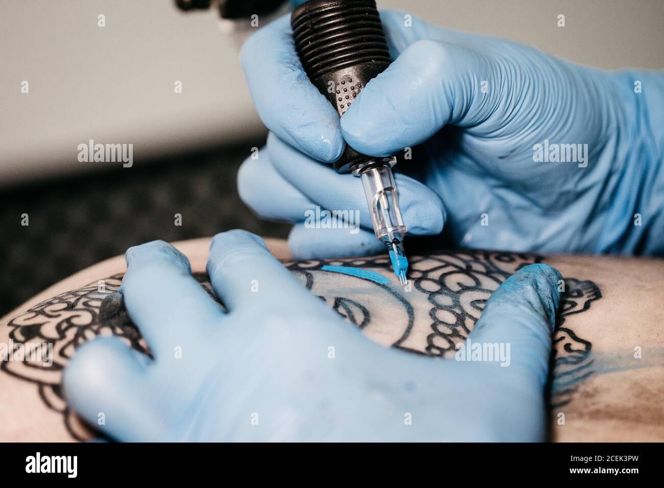 Nahaufnahme der Hände in Latexhandschuhen mit Maschine zu Farbe Tattoo mit blauer Tinte im Studio Stockfoto