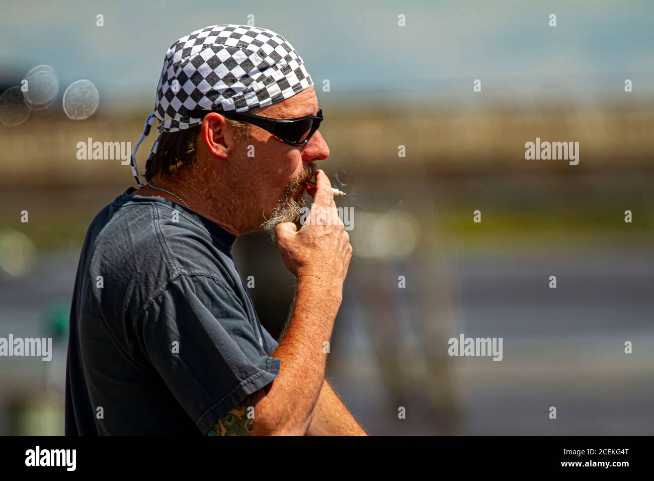 Chestertown, MD, USA 08/30/2020: Profilbild eines kaukasischen Rockers mittleren Alters mit Schachbrettmuster-Bandanna und Sonnenbrille ist rauchig Stockfoto