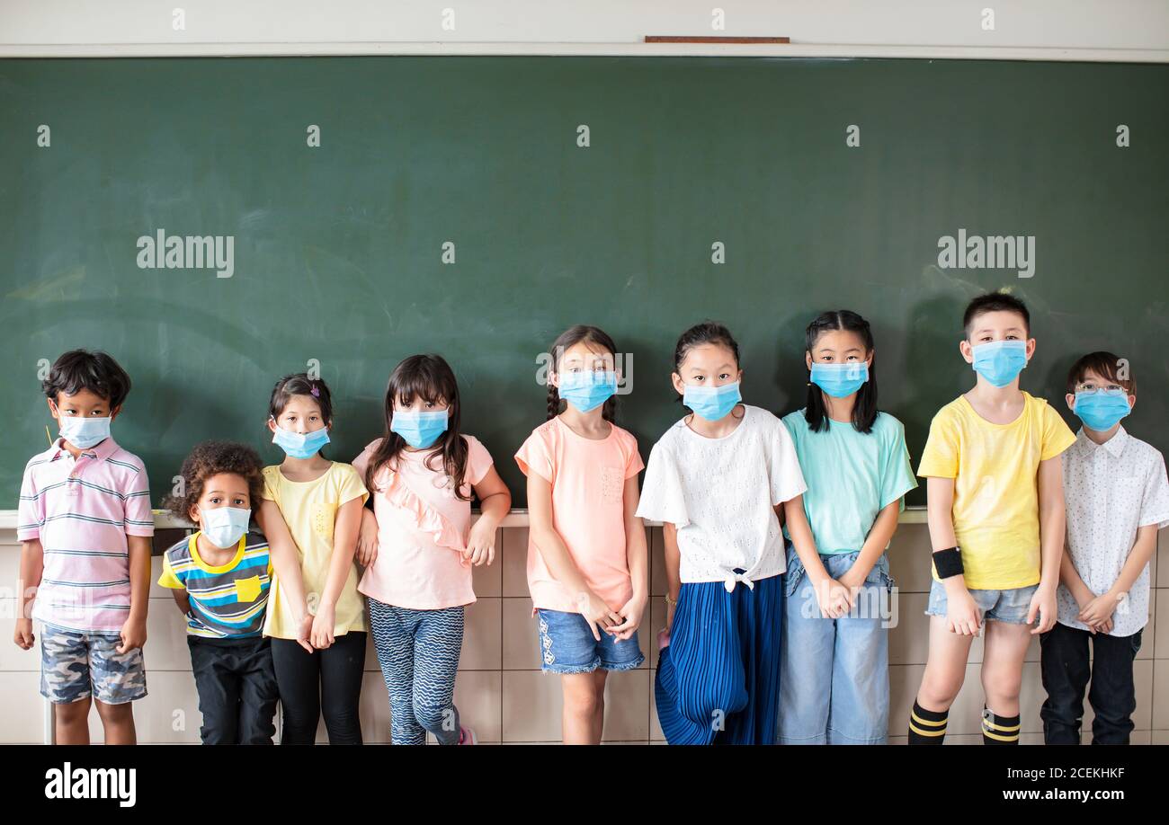 Gruppe von verschiedenen jungen Studenten tragen Maske und stehen zusammen Im Klassenzimmer Stockfoto