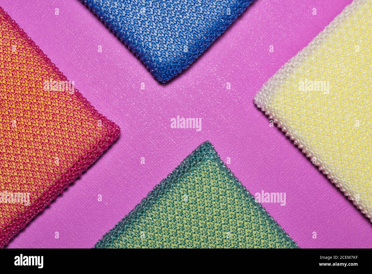 Bunte Putzschwämme in Dreiecksdiagonalen auf einem peony farbigen Hintergrund angeordnet. Lebendiges Vollformatbild. Stockfoto