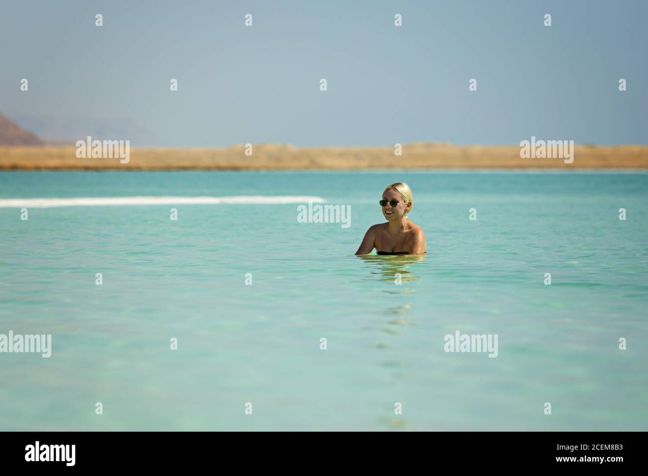 Blonde Frau schwimmt im türkisfarbenen Wasser der Toten Meer Stockfoto