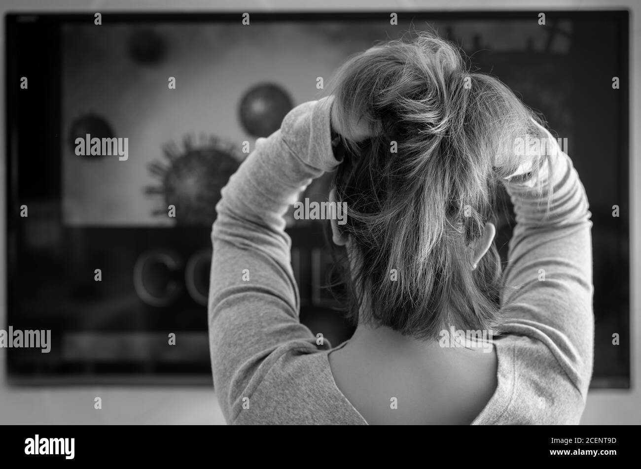 Eine Frau schaut sich ein Fernsehprogramm über die Verteilung von COVID an. Das Konzept eines depressiven Staates. Schwarz-Weiß-Fokus ausgewählt Stockfoto