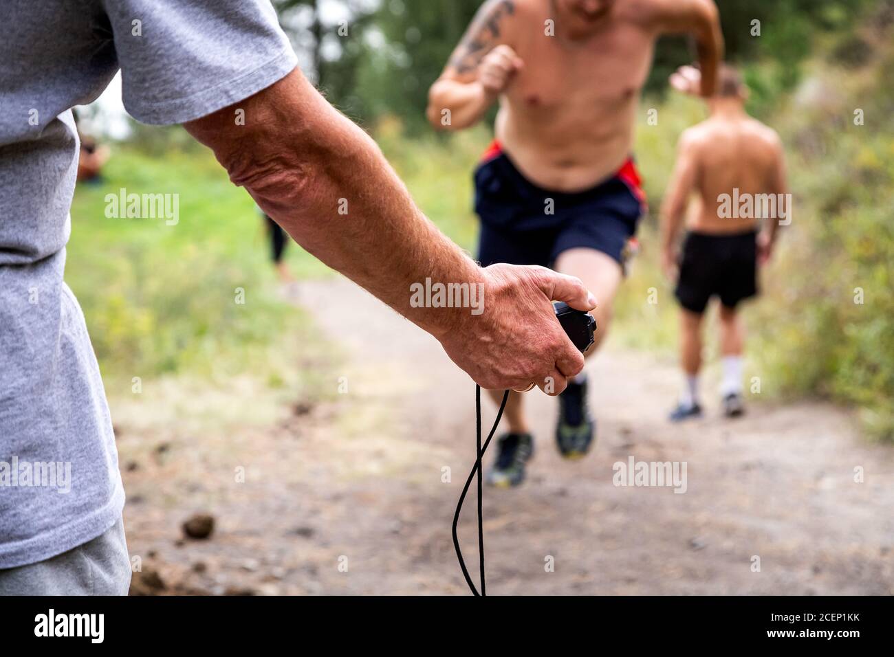 Nahaufnahme eines Trainers hält eine Stoppuhr in der Hand und die Messung der Geschwindigkeit des Kurzstreckens von Athleten, im Hintergrund schöne Natur Stockfoto