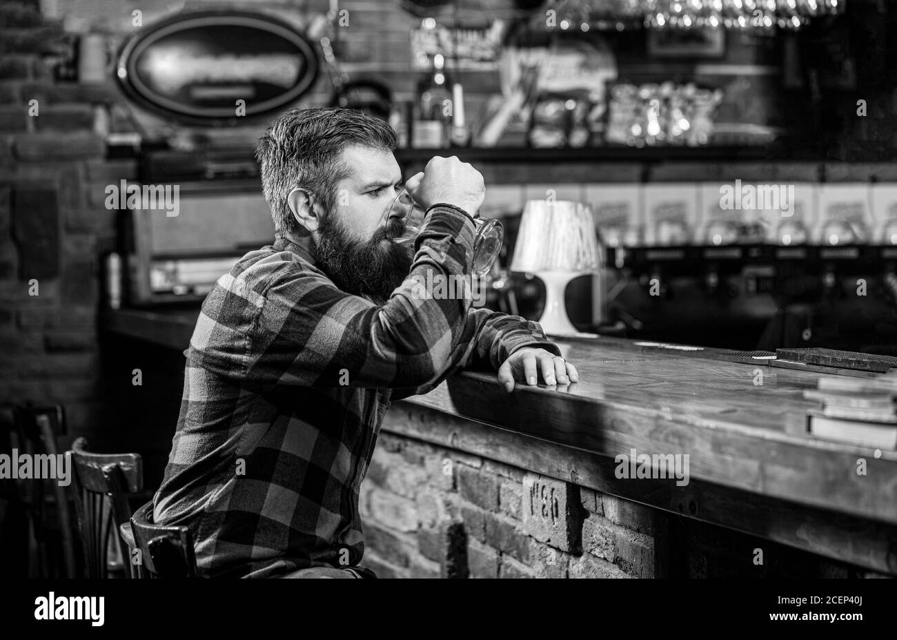 Mann trinkt Bier an der Bar. Mann mit Bier. Bärtiger Hipster hält ein Glas Bier. Bierkneipe. Stilvoller Typ im Cafe Pub. Schwarz und Weiß Stockfoto