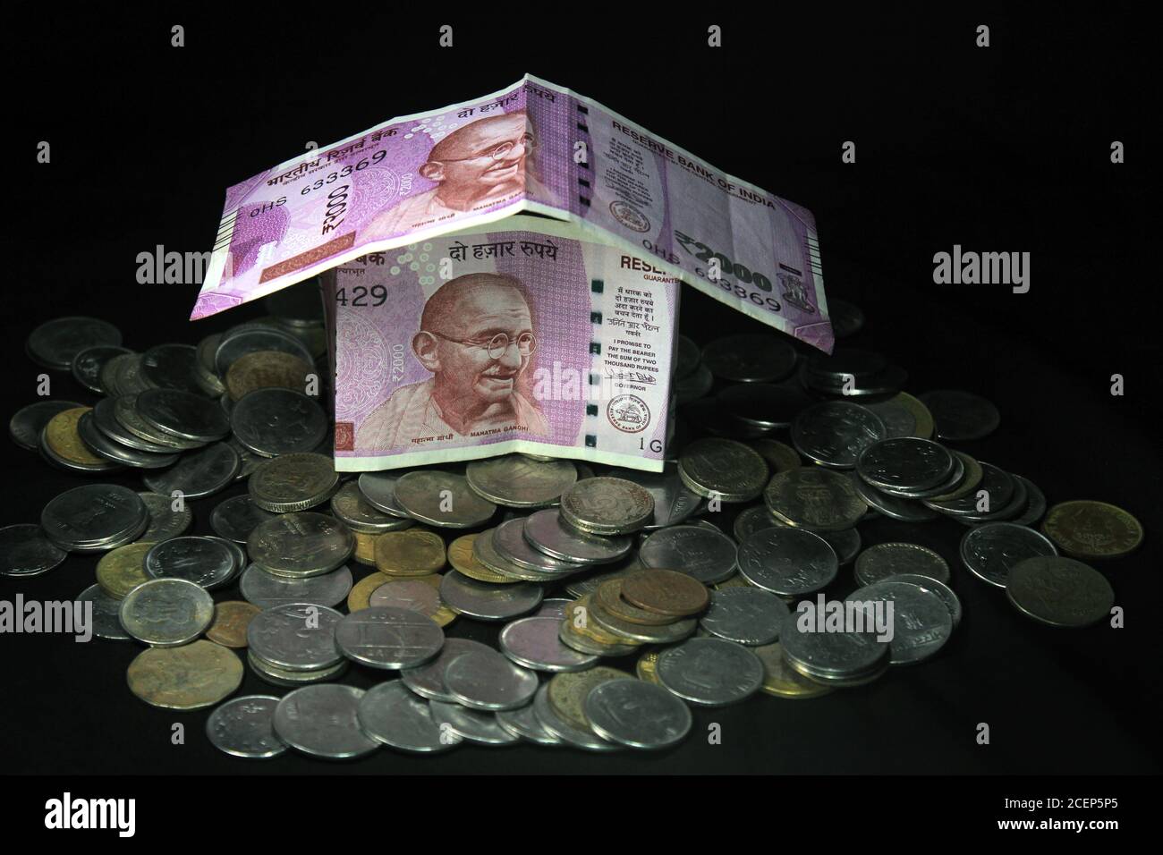Konzept der indischen Rupie Banknoten in Form eines einfachen Hauses auf schwarzem Hintergrund gefaltet. Neue indische Währung. 2000 Rupie-Note mit Münzen. Stockfoto
