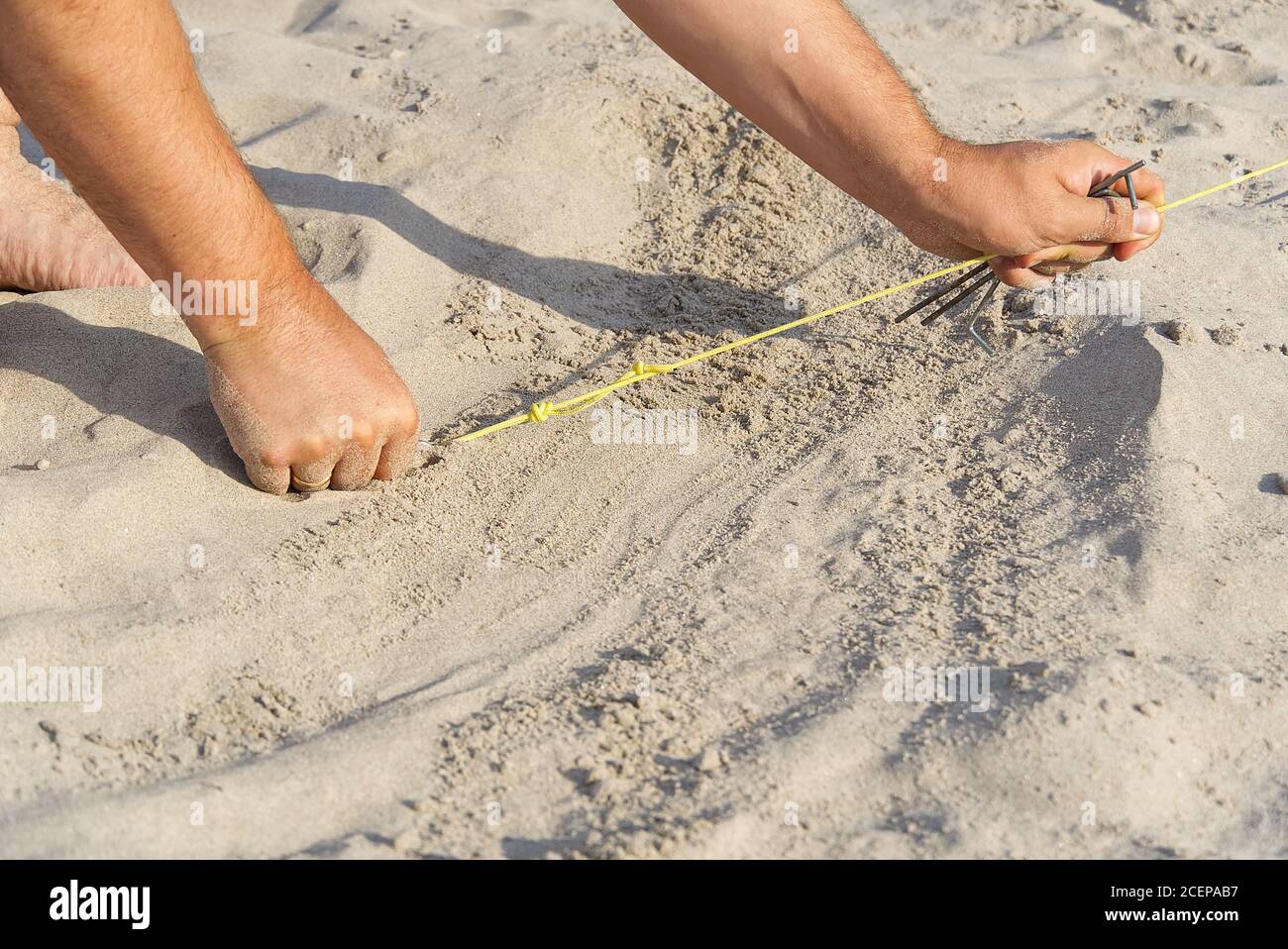 Ein Metallkeil, der in den Sand getrieben wird, um das Seil aus dem Zelt zu ziehen. Camping an einem Sandstrand. Mann hebt ein Zelt am Strand. Natur Reisekonzept. Stockfoto