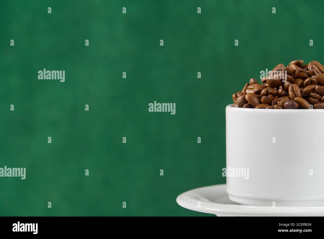Internationaler Tag des Kaffees Konzept. Nahaufnahme weiße Kaffeetasse voller Kaffeebohnen auf dunkelgrünem Hintergrund. Stockfoto