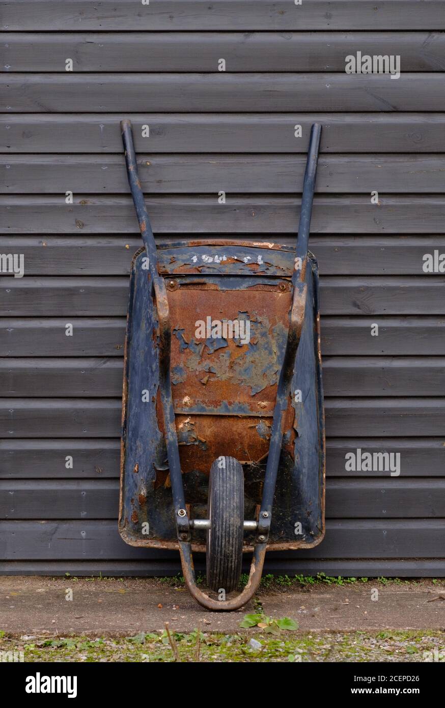 Rusty gebrauchte Schubkarre stand gelehnt an einen Schuppen bereit für die Arbeit. Stockfoto