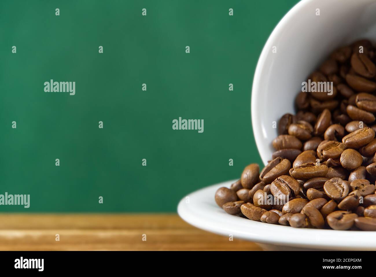 Internationaler Tag des Kaffees Konzept. Nahaufnahme weiße Kaffeetasse voller Kaffeebohnen auf dunkelgrünem Hintergrund. Stockfoto