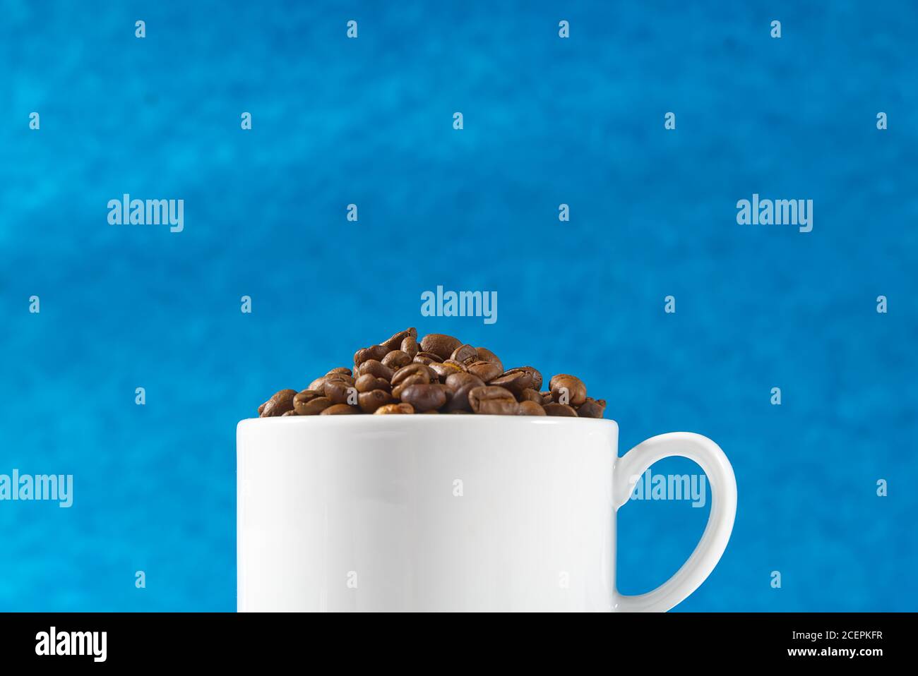 Internationaler Tag des Kaffees Konzept. Nahaufnahme weiße Kaffeetasse voller Kaffeebohnen auf blauem Hintergrund. Stockfoto