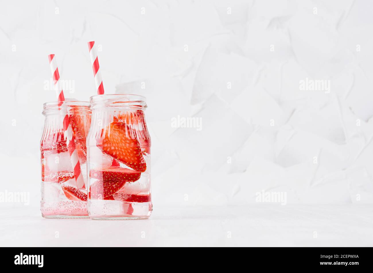 Frische Erdbeer-Limonaden mit Beere in Scheiben, Sodawasser, Eiswürfel mit Stroh in transparenten Gläsern auf einem weichen hellen weißen Holztisch, Kopierraum. Stockfoto