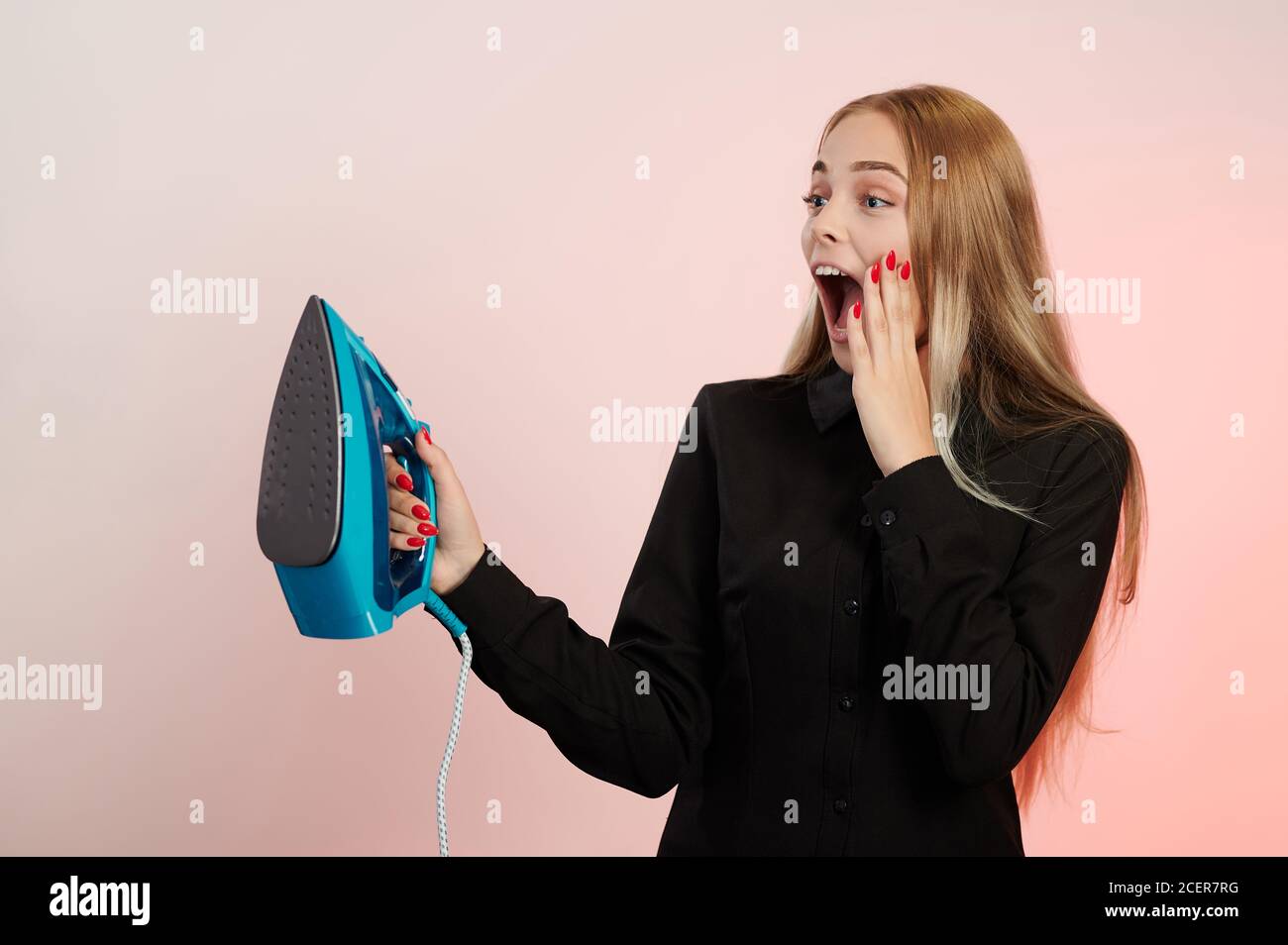 Schreiende junge Mädchen mit Eisen in der Hand isoliert auf rosa Hintergrund Stockfoto