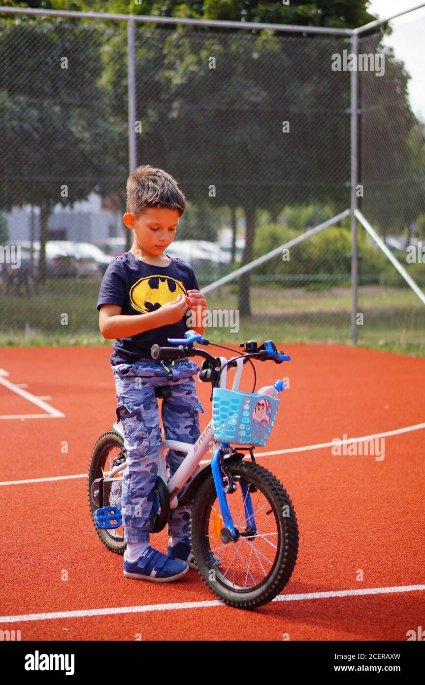 POZNAN, POLEN - 30. Aug 2020: Kleiner Junge mit einem Batman-Hemd auf einem Fahrrad auf einem Sportplatz sitzend Stockfoto