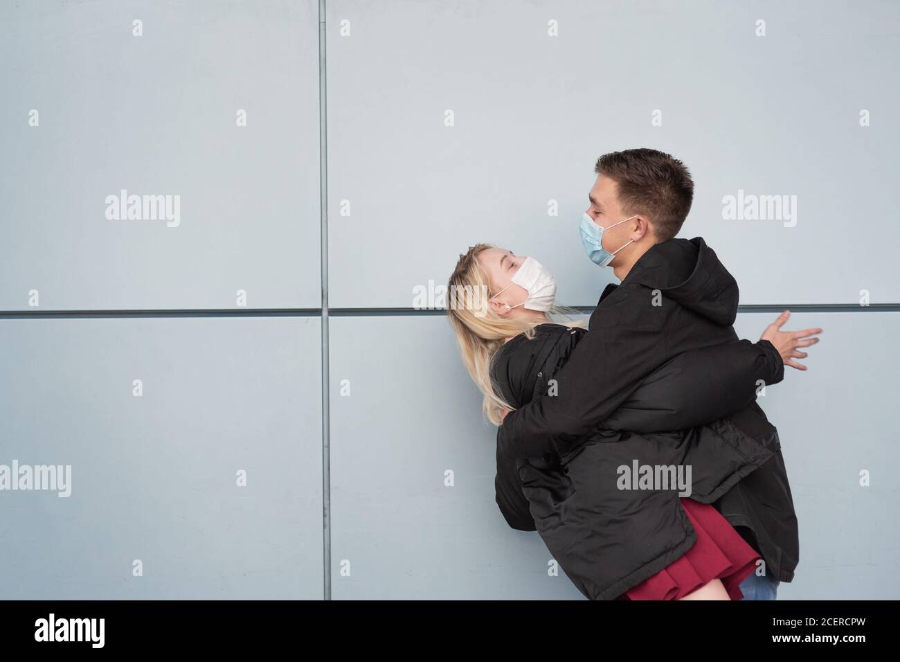 Junges, glückliches, liebevolles Paar, das Masken trägt, sich umarmt und einander in die Augen starrt Stockfoto