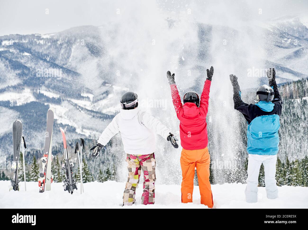 Rückansicht von Freunden Skifahrer in Skianzügen und Helmen werfen frischen Pulverschnee hoch in die Luft, Spaß auf verschneiten Hügel mit schönen Bergen im Hintergrund. Konzept von Skigebiet und Freundschaft. Stockfoto