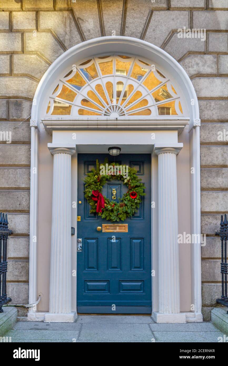 Blaue Georgianische Tür, geschmückt zu Weihnachten mit grünen Kranz und roten Dekorationen. Dublin, Irland. Holzeingang mit Steinsäulen und Fanlight Stockfoto