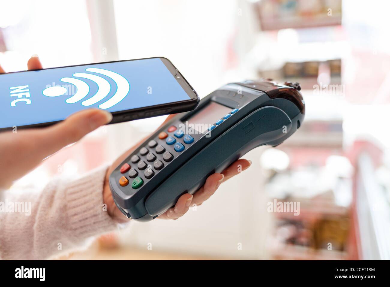Die Hände einer Frau halten ein Zahlungsterminal und bezahlen für einen Kauf mit einem Smartphone.auf dem Telefon-Bildschirm, das wi-Fi-Netzwerk. Das Konzept von NFC, Stockfoto