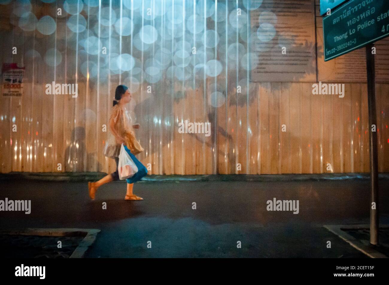 Eine Thai-Dame macht sich auf den Weg an einer Baustelle entlang der durchnässten, regnerisch durchnässten Sukhumvit Rd. Bangkok, Thailand. Stockfoto