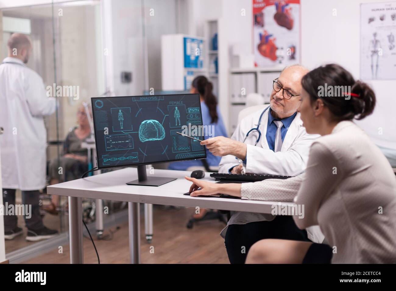 Reifer Arzt erklärt Röntgen für junge Frau Patienten im Krankenhaus-Büro und die Behandlung von Hirnverletzungen. Junge Sanitäter im weißen Mantel sprechen über Krankheit Diagnose mit behinderten älteren Frau im Rollstuhl. Stockfoto