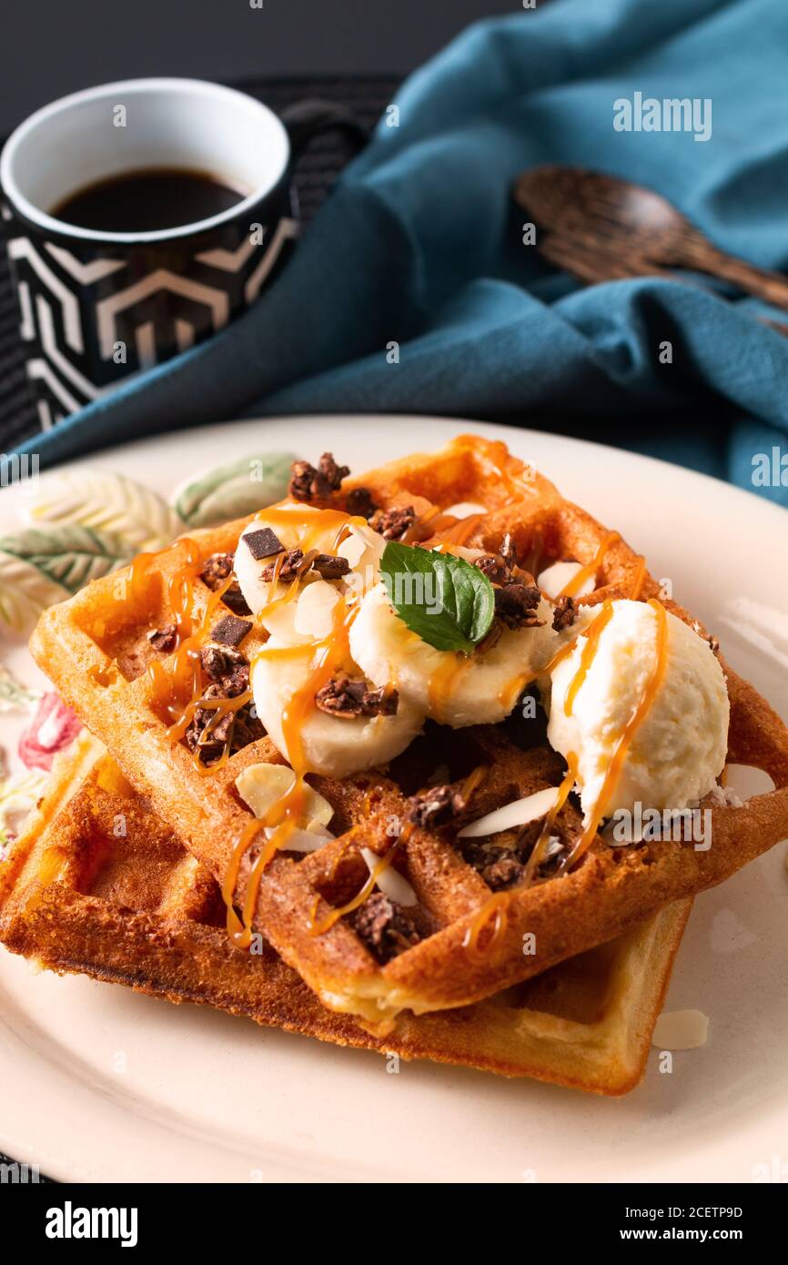 Essen Essen Frühstück Konzept hausgemachte Bio-Waffeln Banane Vanille Eis Belag mit Karamellsauce auf schwarzem Hintergrund mit Kopierraum Stockfoto