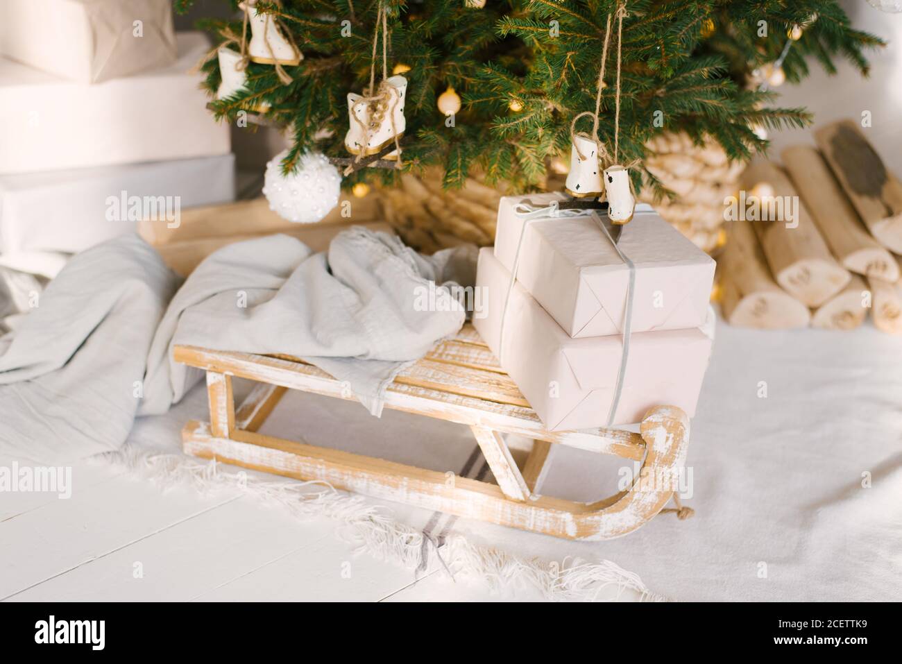 Holzschlitten mit Decke und Geschenken unter dem Weihnachtsbaum. Weihnachtsdekor im Inneren des Hauses Stockfoto