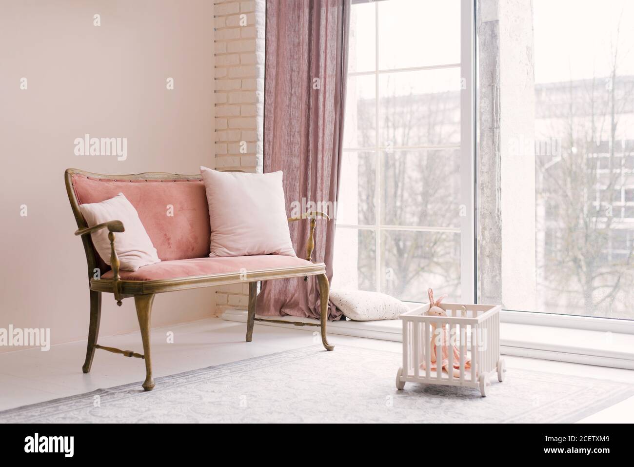 Ein rosa Vintage Sofa mit Kissen steht neben dem Fenster im Wohnzimmer oder Kinderzimmer im Haus. Minimalistisches Innendesign Stockfoto