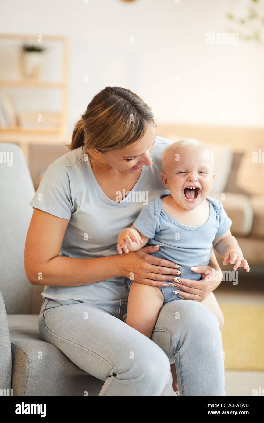 Vertikale Aufnahme von liebevoller Mutter im Sessel sitzen und haben Spaß mit ihrem kleinen
