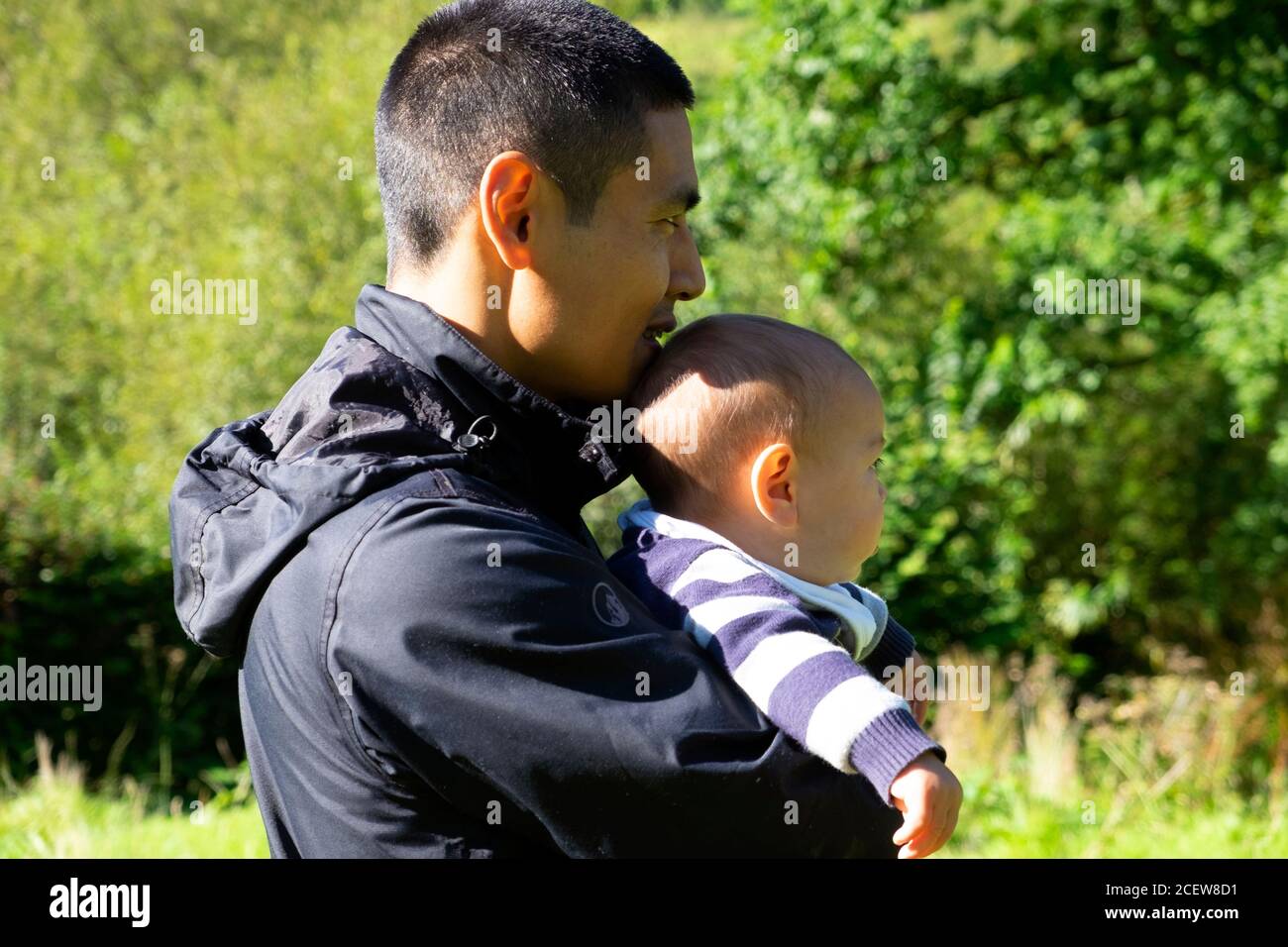 Asiatische Mann 30s Profil Seitenansicht halten Kind Baby Sohn 6 Monate trägt Anorak auf dem Land Wales UK KATHY DEWITT Stockfoto