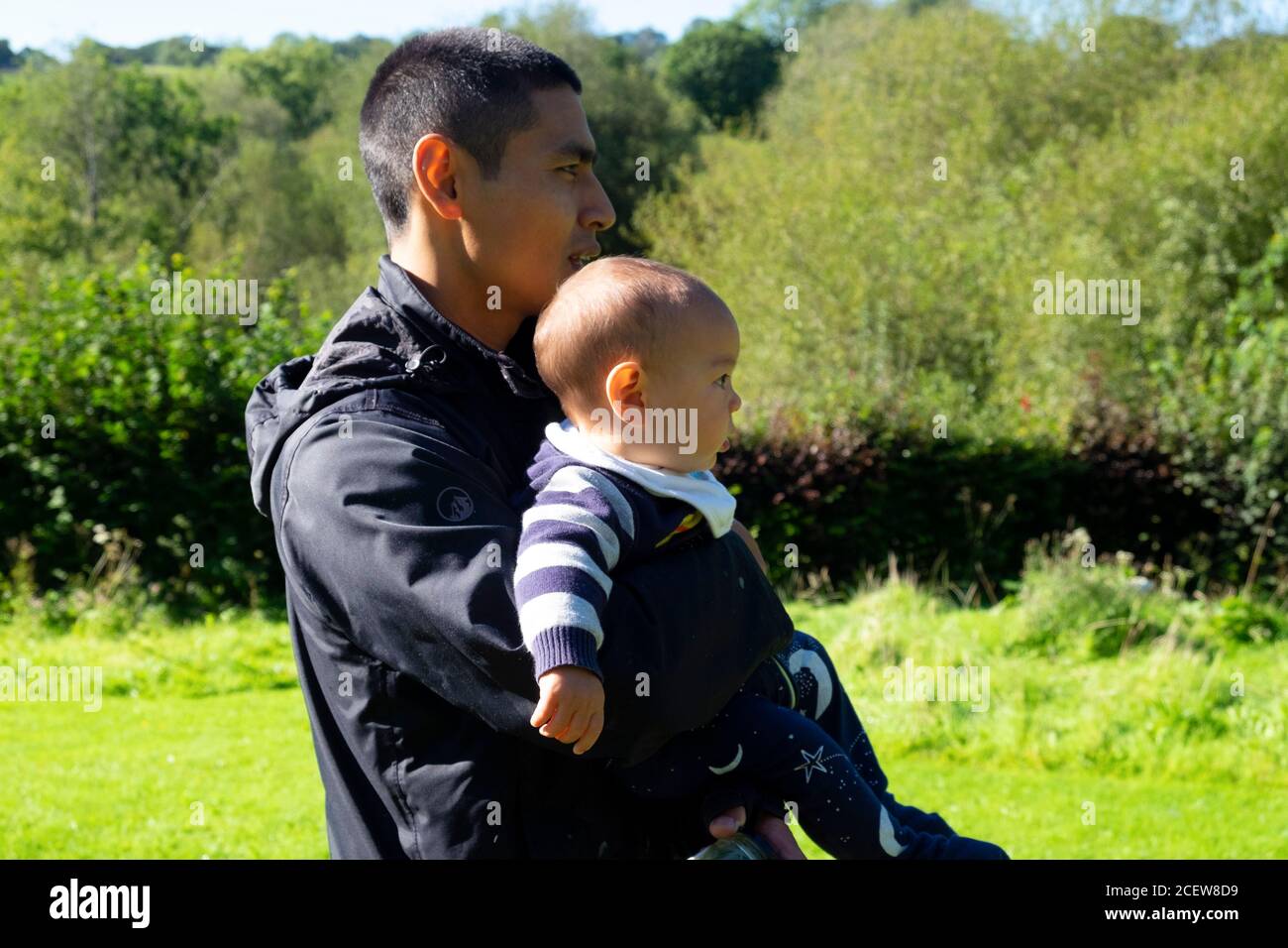 Asiatische Mann 30s Profil Seitenansicht halten Kind Baby Sohn 6 Monate trägt Anorak auf dem Land Wales UK KATHY DEWITT Stockfoto