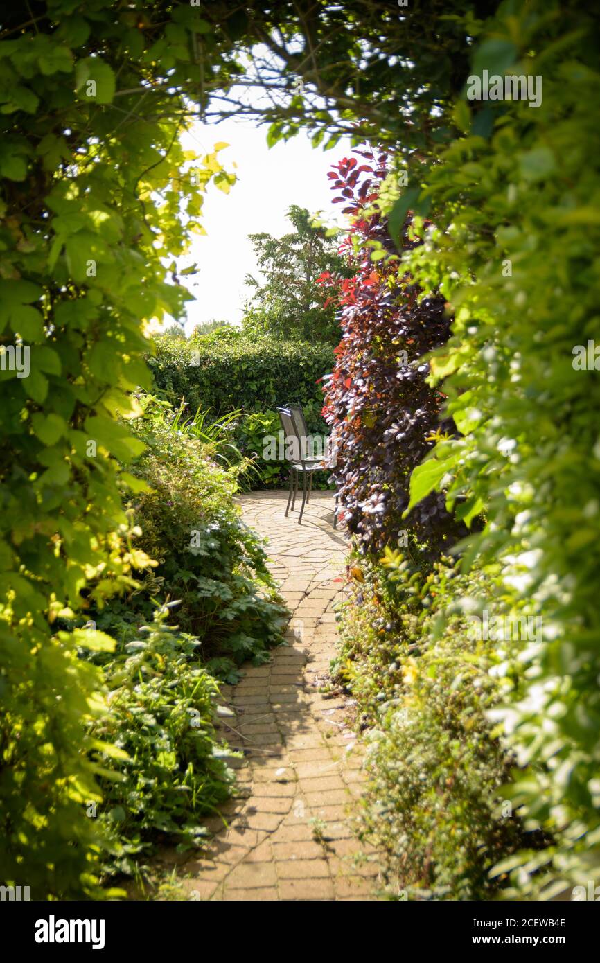 Ein englischer Cottage geheimen Gartenweg führt unter Bogen zu Ein privater Tisch und Stühle in der warmen Sommersonne Stockfoto