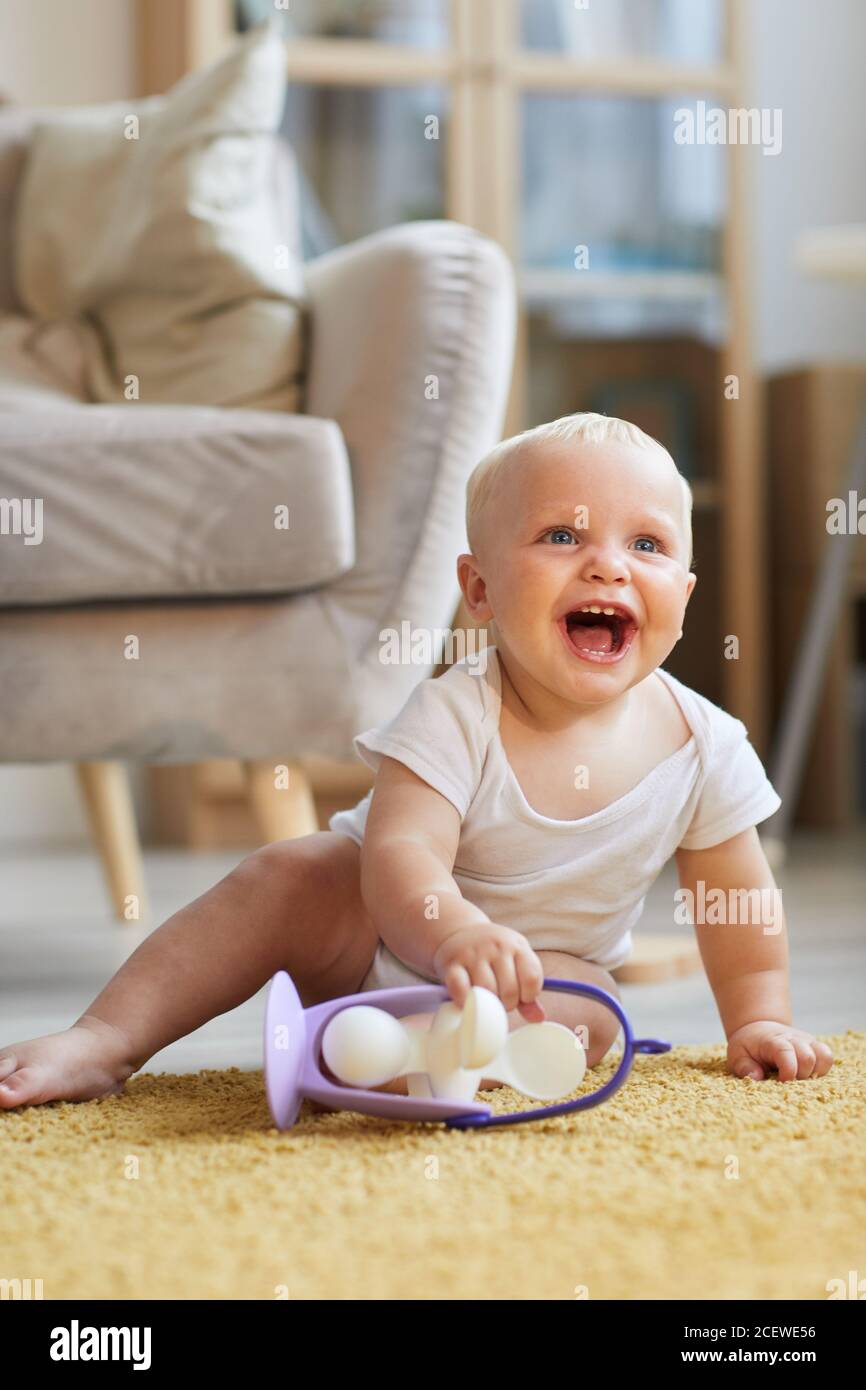 Vertikale Aufnahme von glücklich verspielt Baby Junge auf dem Boden sitzen Im Wohnzimmer spielen mit Spielzeug und lachen Stockfoto