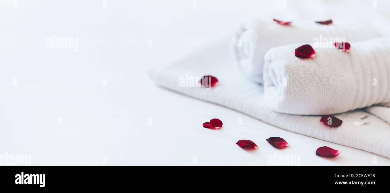 Luxuriöses Hotelzimmer mit weißen Spa-Handtüchern auf Bettlaken mit Rosenblättern. Romantisches Urlaubswochenende mit Wellness-Körperbehandlung und Relax-Paarmassage Stockfoto