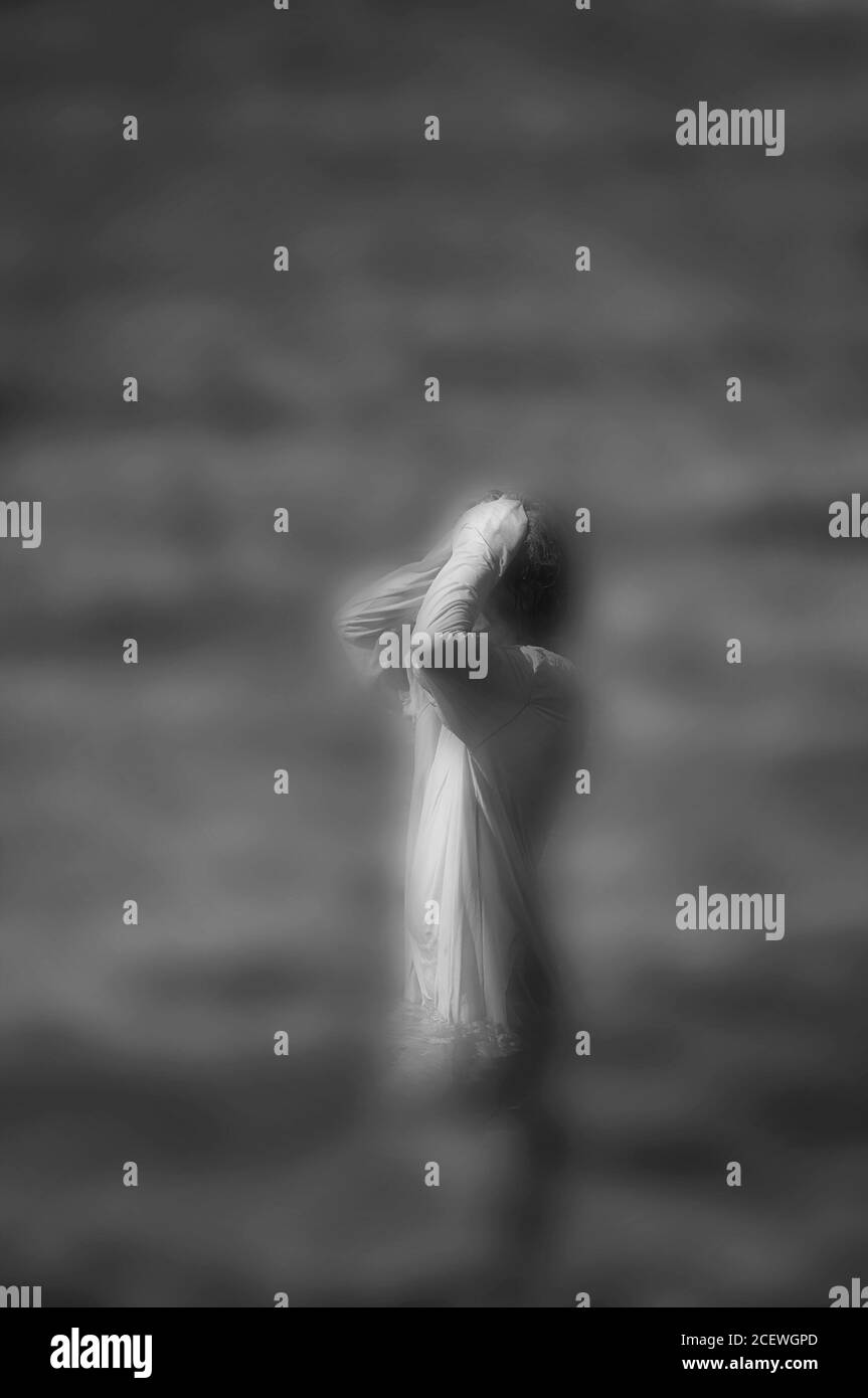 Surreal verschwommenes Schwarz-Weiß-Bild einer unkenntlich stehenden Frau im Wasser. Stockfoto