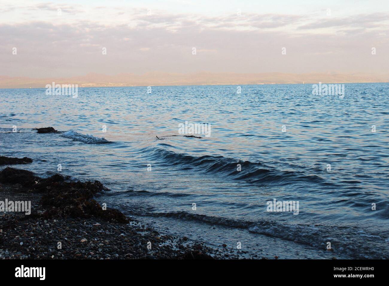 Nahaufnahme von kleinen Wellen, die bei Sonnenuntergang am Pwllheli Beach in Nordwales in die Küste Rollen Stockfoto