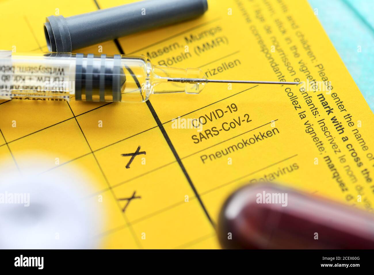 Spritze und Blutabnahmeröhrchen auf Impfkarte, Corona-Impfung Stockfoto