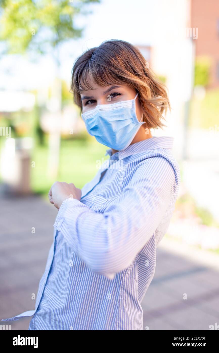 Junge Frau in Maske Gruß mit Ellbogen im Freien im Park Während einer Pandemie Stockfoto