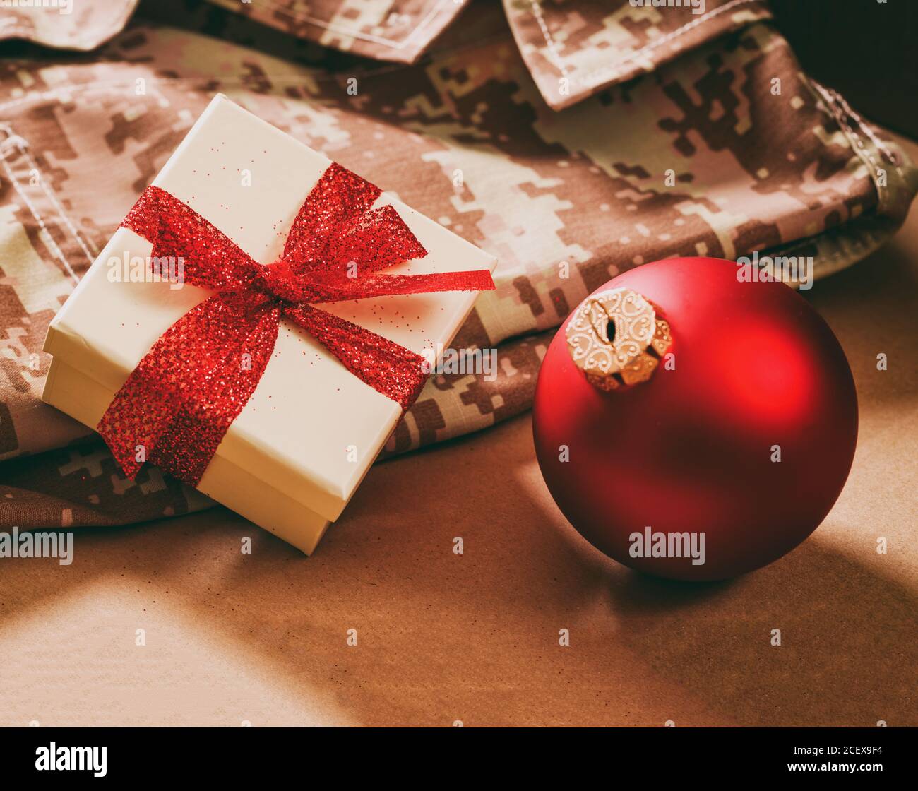 Weihnachten in der Armee. Roter Weihnachtsball und Geschenkbox auf US-amerikanischer Militäruniform, Nahaufnahme Stockfoto