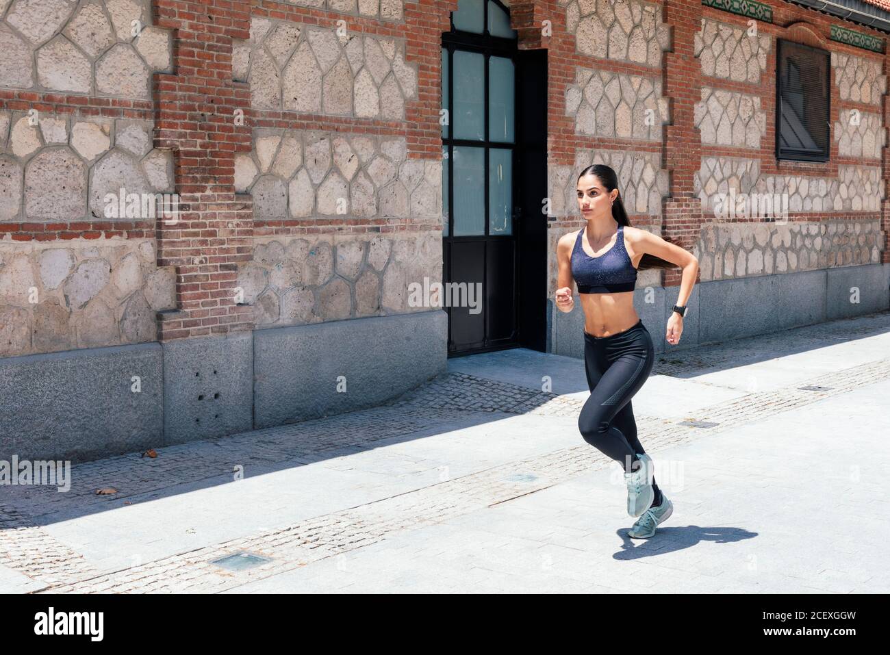 Seitenansicht der frauen Sportbekleidung, die schnell mitläuft Bürgersteig während des Trainings an sonnigen Tagen in der Stadt Stockfoto