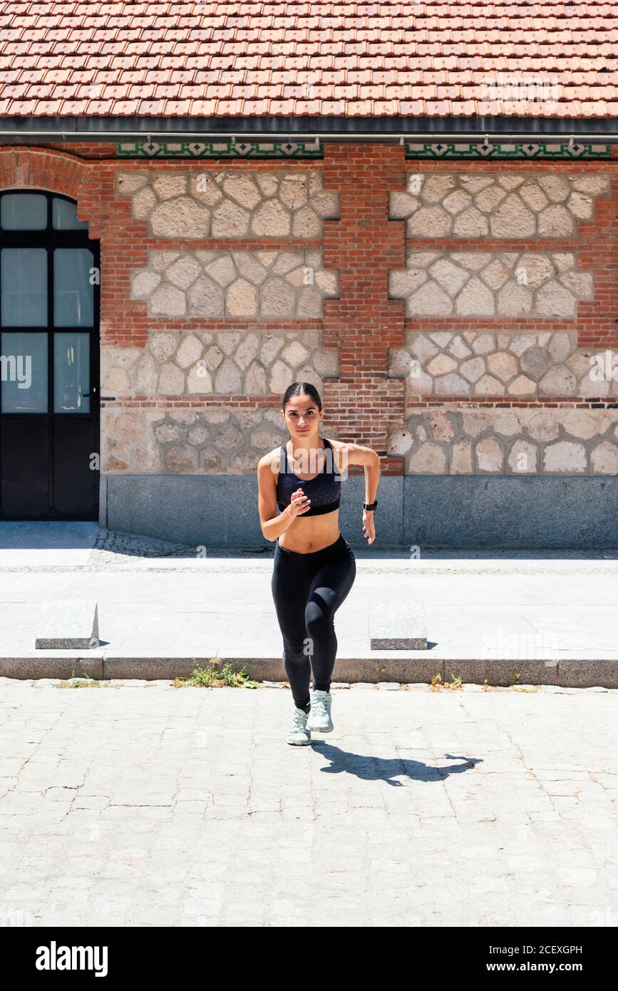 Fit weiblich in Sportbekleidung laufen schnell entlang Bürgersteig während des Trainings An sonnigen Tag in der Stadt Stockfoto