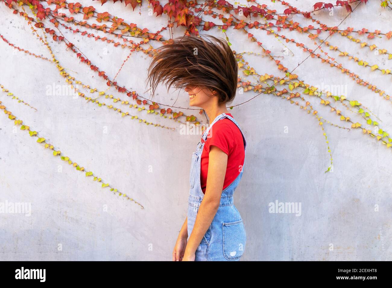 Seitenansicht der jungen fröhlichen Frau mit fliegenden Haaren stehend In der Nähe der Steinmauer Stockfoto