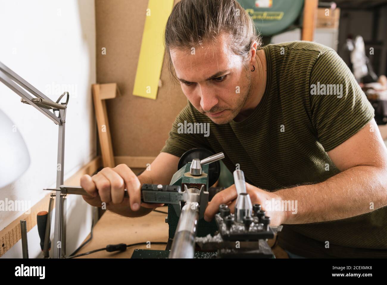 Schöner männlicher Holzarbeiter, der an der Werkbank steht und Details misst Bremssattelwerkzeug während der Arbeit in der Werkstatt Stockfoto