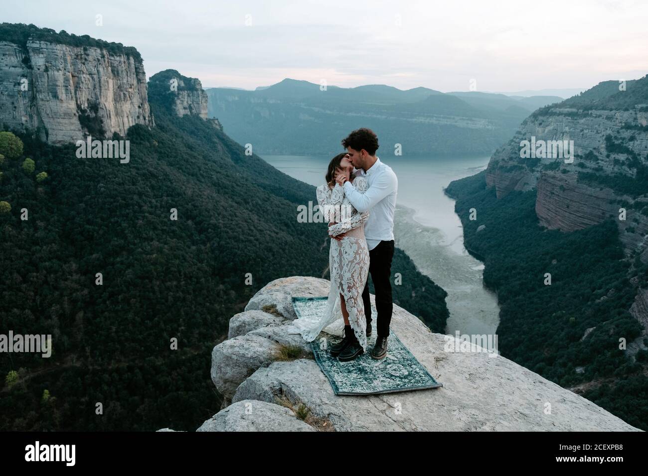 Seitenansicht eines jungen Mannes und einer Frau in eleganter Kleidung, die auf einer felsigen Klippe von Morro de Labella stehen und sich umarmen und sich sanft küssen Stockfoto