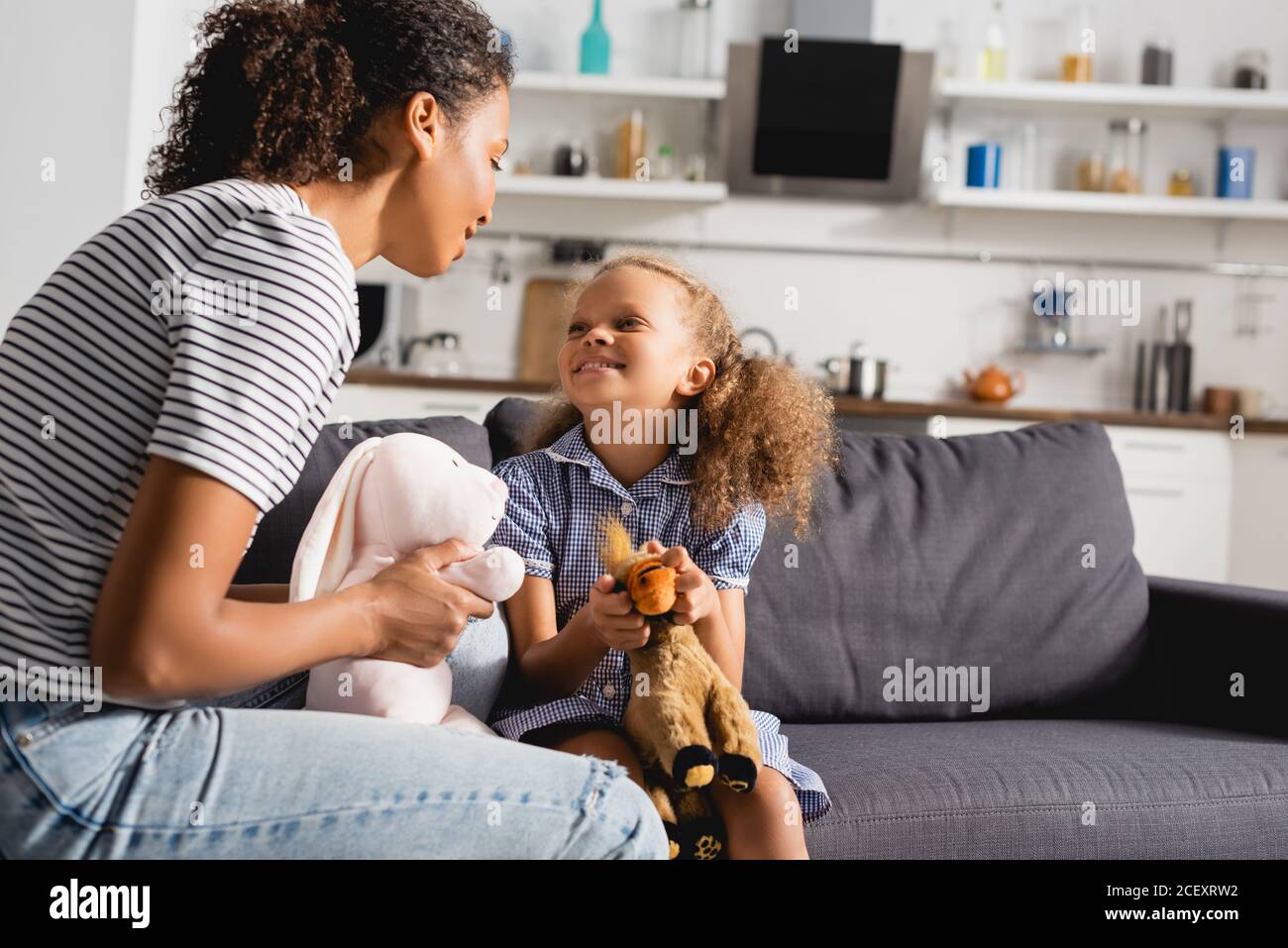 afroamerikanische Kindermädchen und Babysitter halten Spielzeug beim Betrachen Einander in der Küche Stockfoto