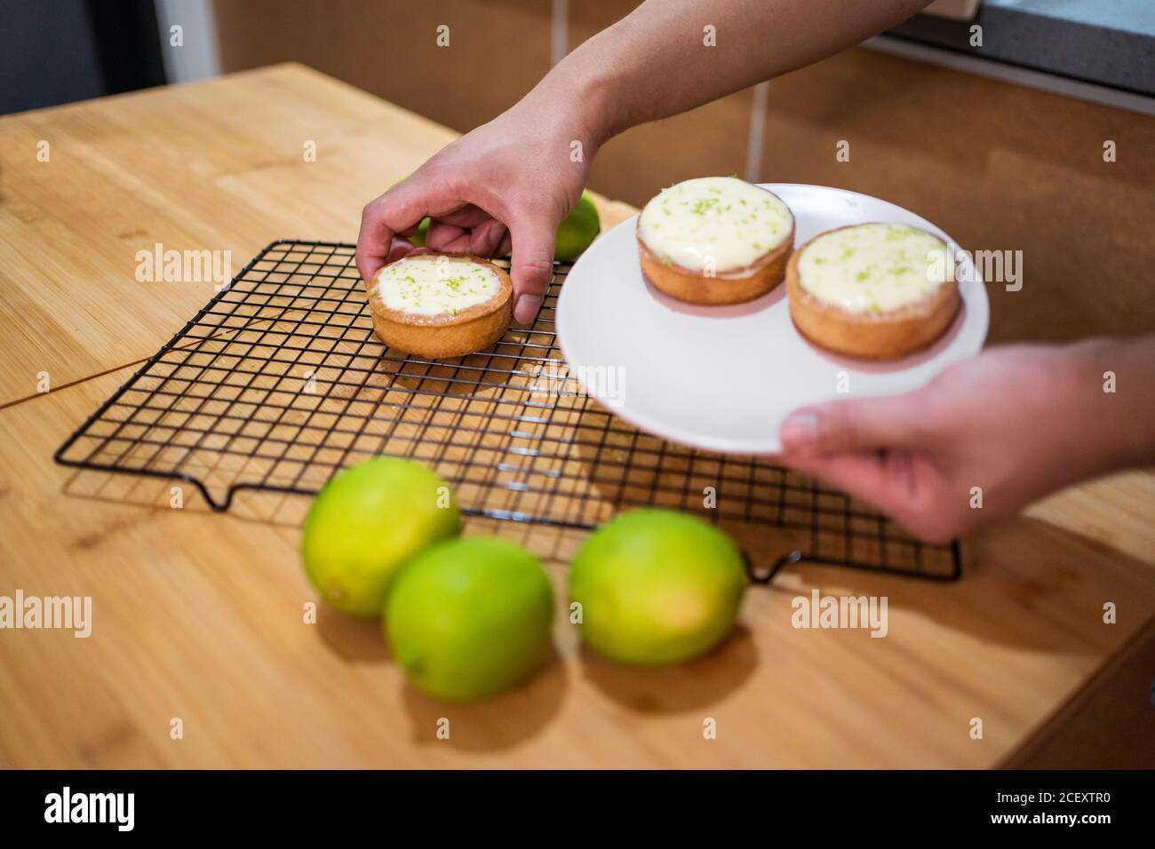 Gesichtslose Person, die köstliche Limettensorten mit Sahne auf Weiß arrangiert Platte über Holztisch Stockfoto