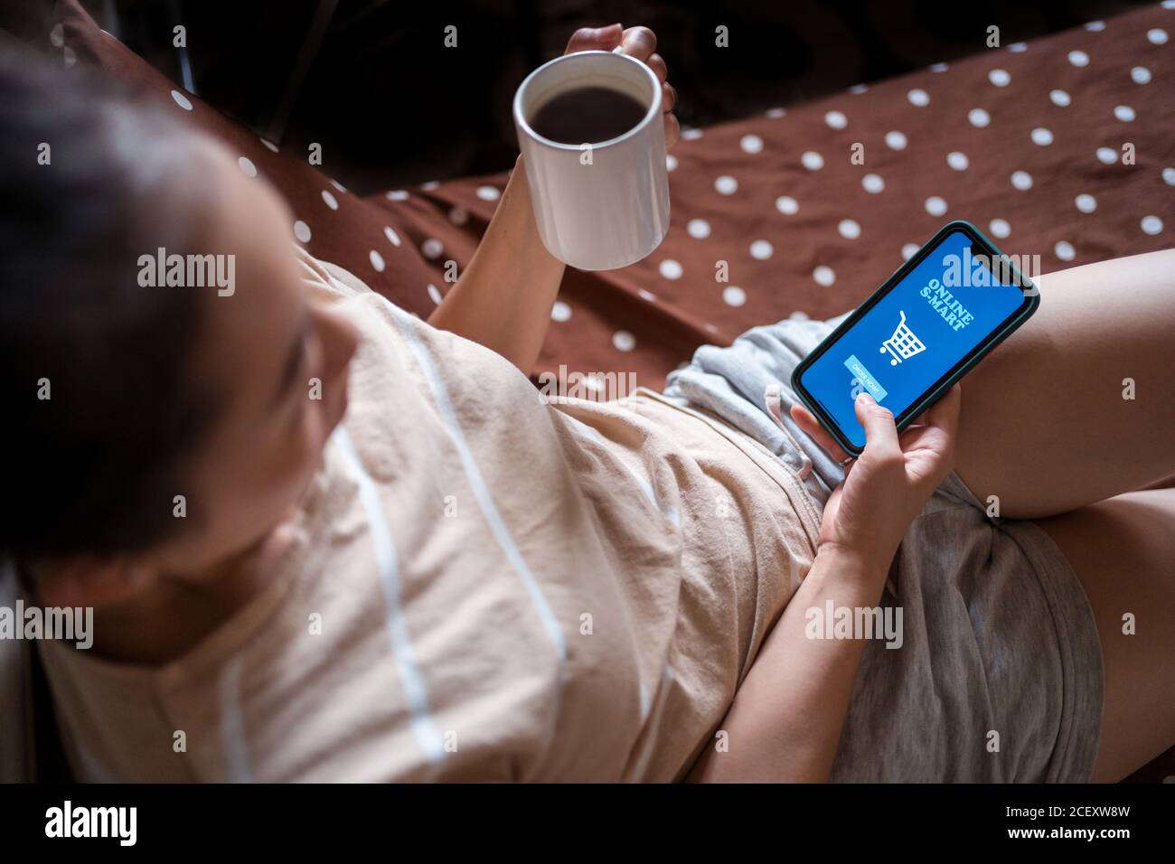 Von oben des Weibchens in der häuslichen Kleidung sitzend auf dem Bett Und Bestellung von Lebensmitteln online während der Verwendung von Handy Stockfoto