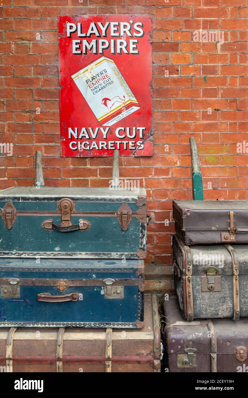 Vintage-Gepäck unter einem Zigarettenplakat an der Bluebell Railway, Heritage Railway Line, Horsted Keynes Station, West Sussex, Großbritannien gestapelt Stockfoto