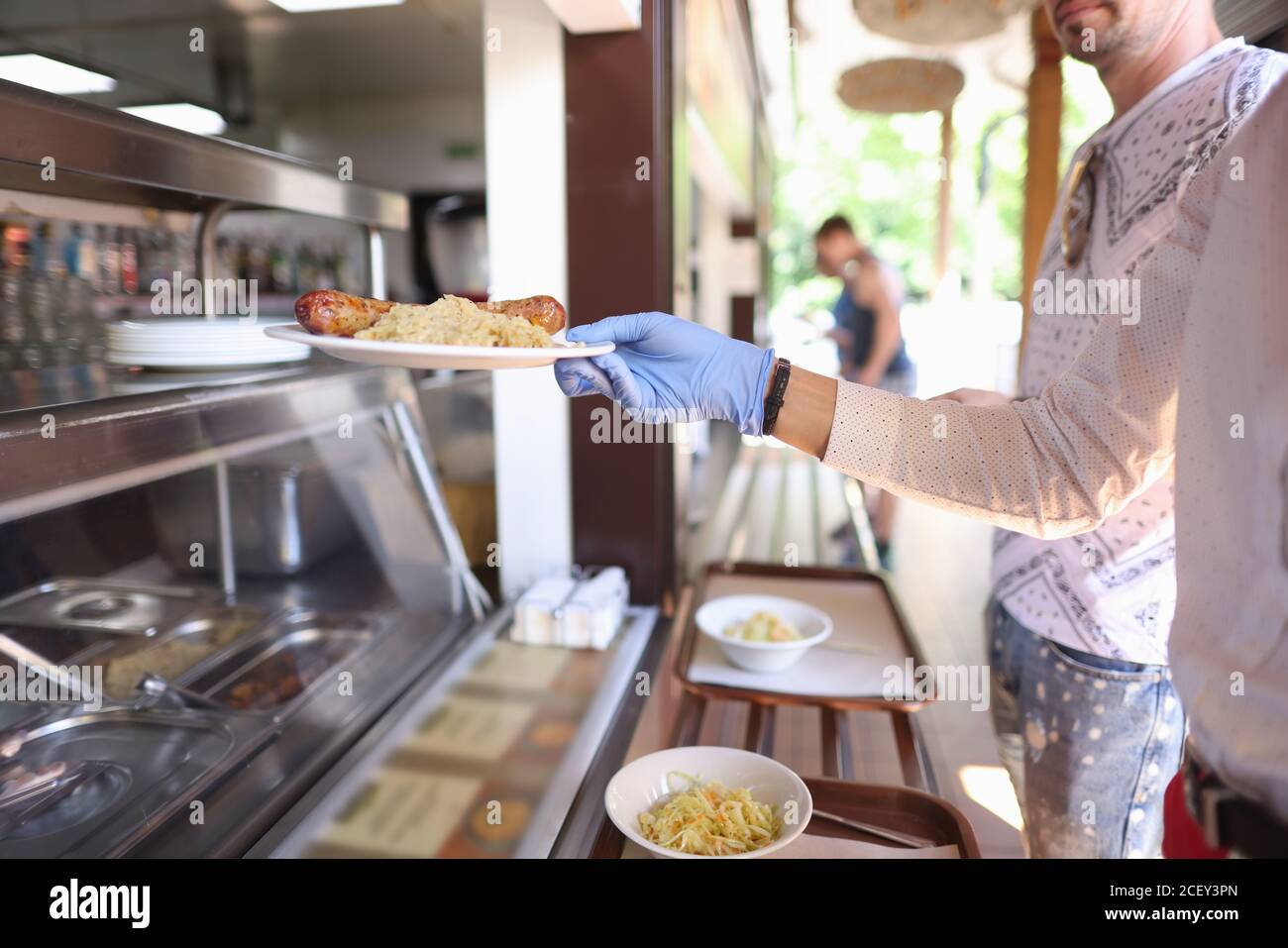 Frau in Handschuhen steht im Bistro und greift Teller des Abendessens. Stockfoto