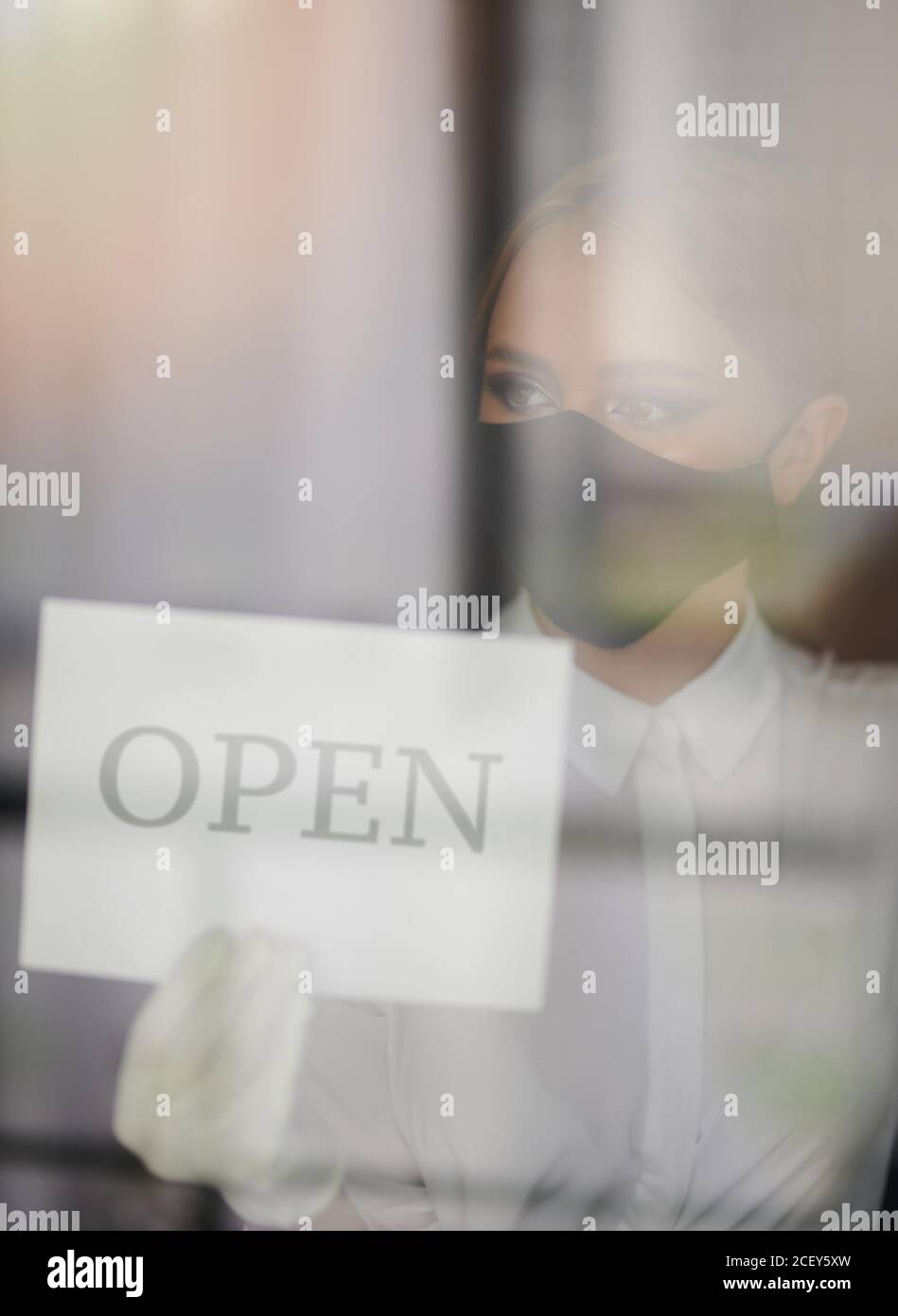 Junge Frau in Gesichtsmaske öffnen Geschäft nach Lockdown Stockfoto