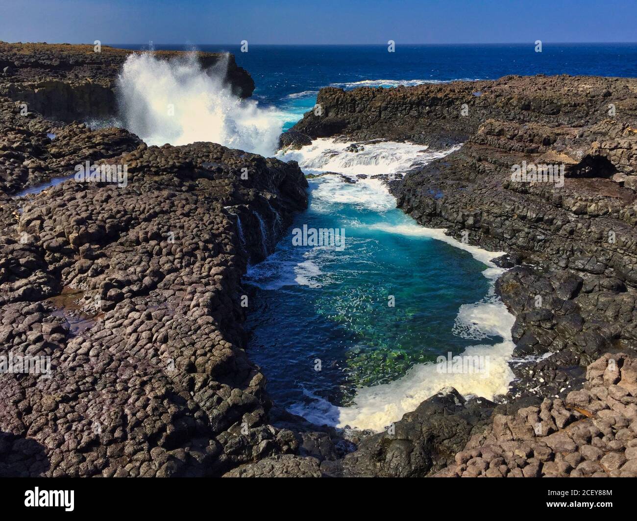 Buracona - das Blaue Auge von Cabo Verde - blau Lagune in einem schwarzen Felsen mit Meer spritzen in der Zurück Stockfoto
